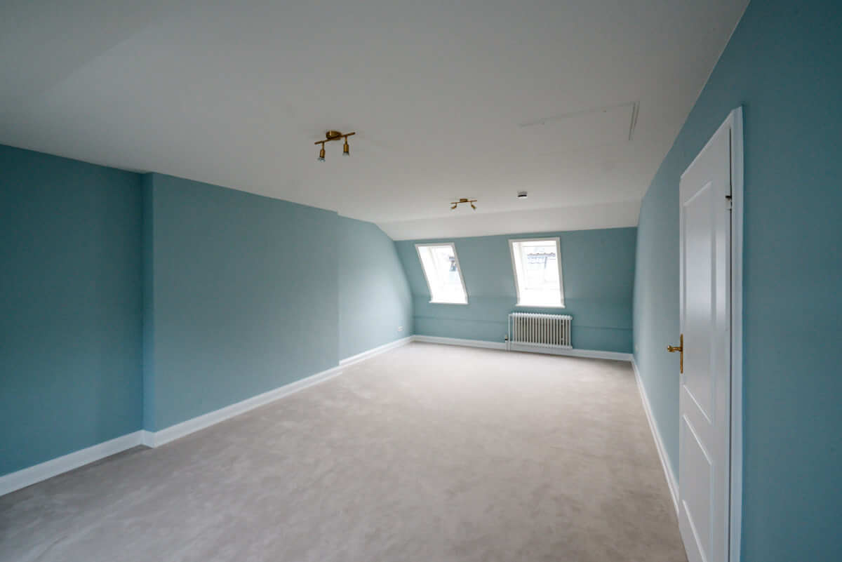 Blaue Farbe und ein neuer heller Teppich in einem Dachbodenzimmer